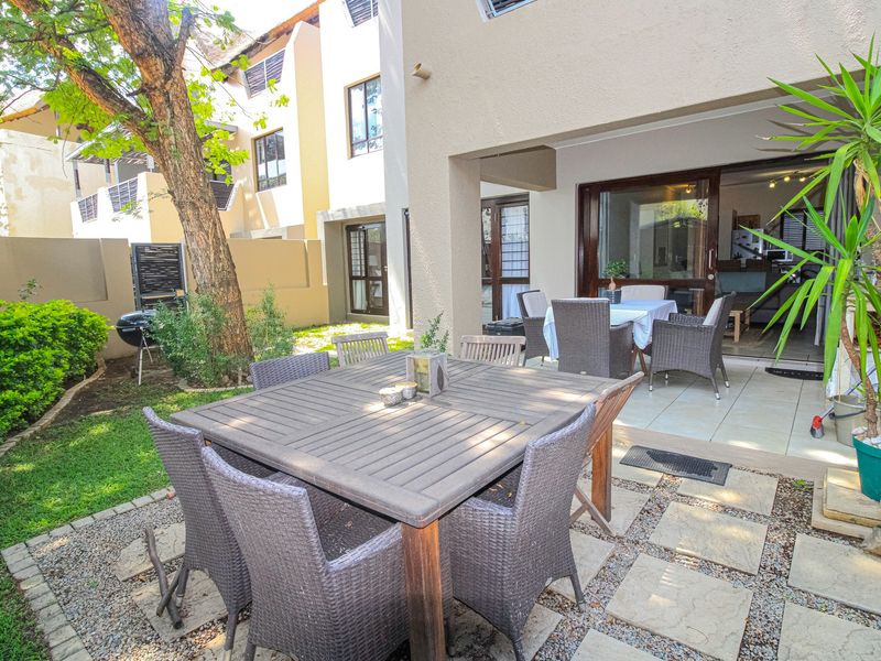 A private rear patio area featuring tiled flooring and direct access to the interior living space, complemented by a landscaped garden and paved seating area.