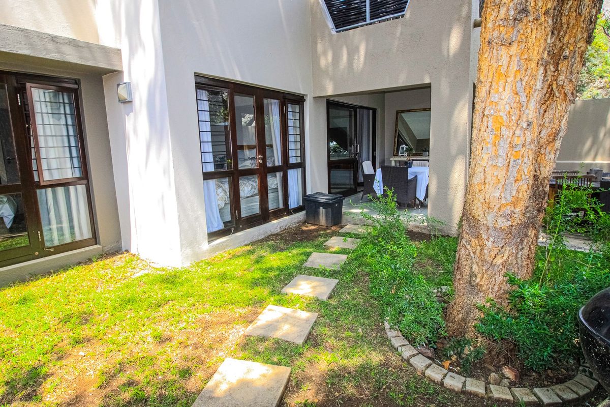 Rear view of the apartment featuring a covered patio, paved garden path, and large timber-framed windows providing access to the interior living spaces.