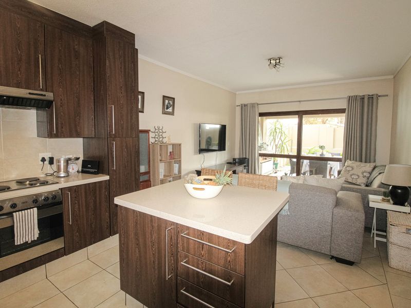 Open plan kitchen and living area featuring dark wood cabinetry, a central island, tiled flooring, and direct access to an outdoor patio space.