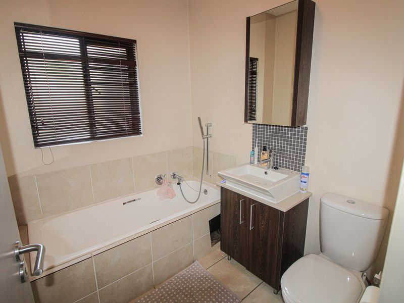 A functional bathroom featuring a built-in bathtub with tiled surround, a vanity cabinet with basin, a wall-mounted mirror cabinet, and a standard toilet.