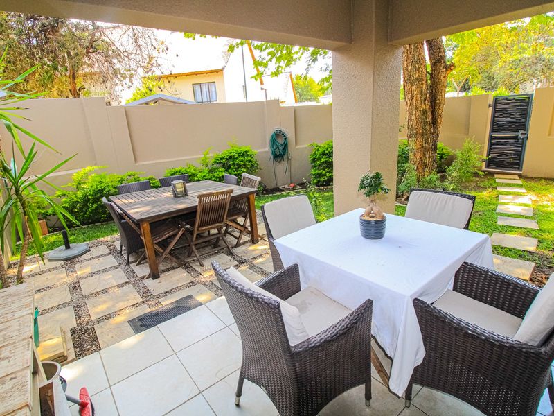 A covered patio area featuring tiled flooring and a paved outdoor space, overlooking a private garden with boundary walls.