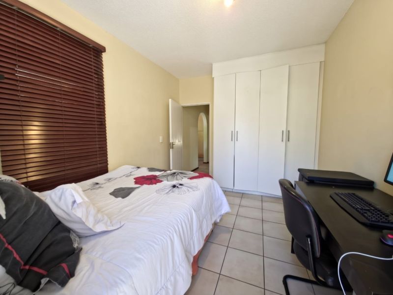 A functional bedroom featuring built-in cupboards, tiled flooring, and venetian blinds, offering a practical layout for comfortable living.