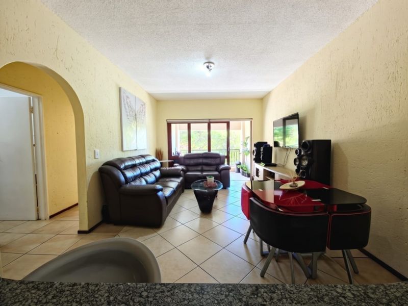 Open-plan living and dining area featuring tiled floors, textured walls, and an arched entryway leading to a balcony with natural light.