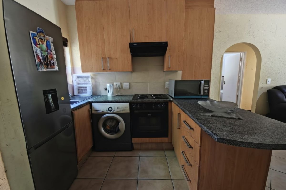 Compact kitchen featuring laminate cabinetry, granite countertops, built-in oven, gas hob, and extractor fan, with tiled flooring and an arched entryway.
