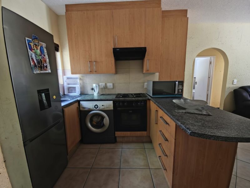 Compact kitchen featuring laminate cabinetry, granite countertops, built-in oven, gas hob, and extractor fan, with tiled flooring and an arched entryway.