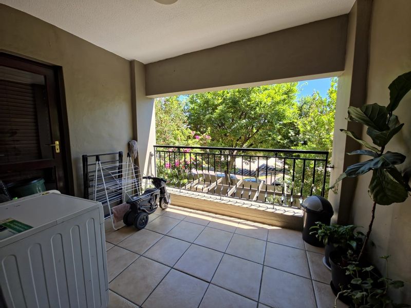 A covered balcony featuring tiled flooring and a metal balustrade, offering an outdoor space with views of surrounding greenery.