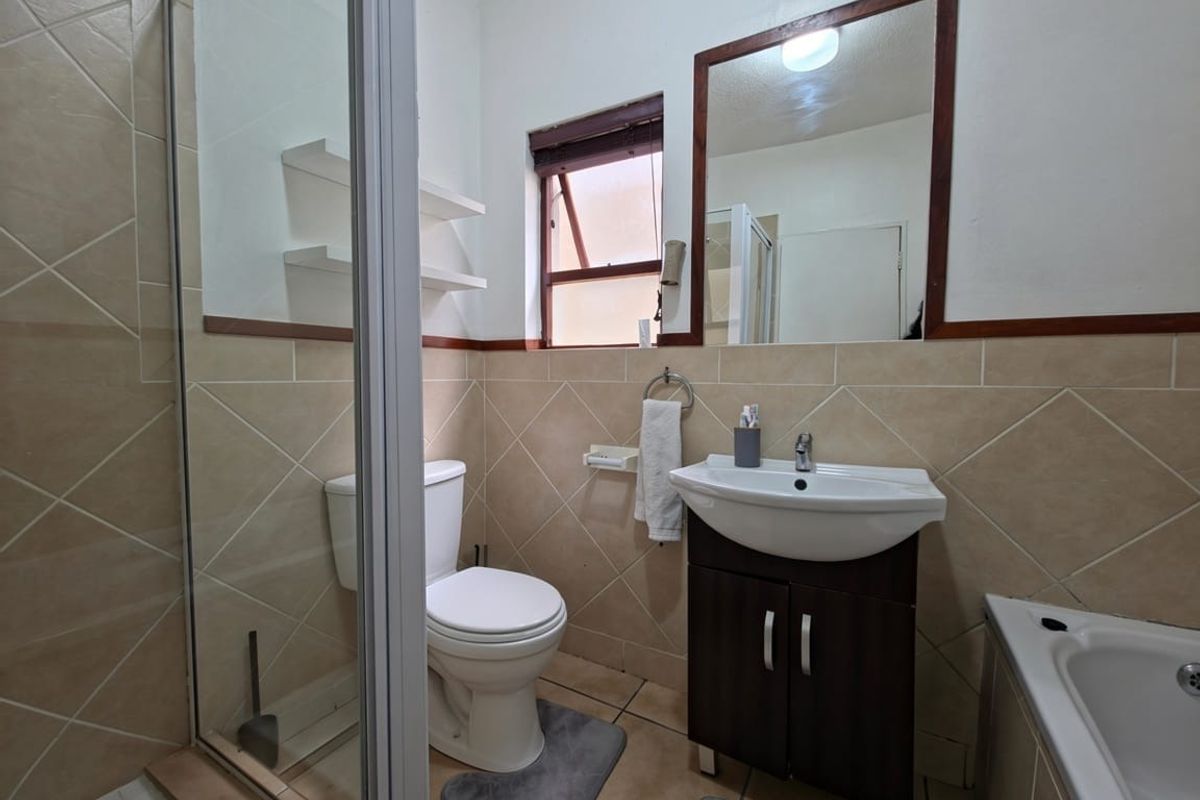 A functional bathroom featuring a shower enclosure, bathtub, vanity cabinet with basin, and tiled finishes, offering a practical layout for daily use.