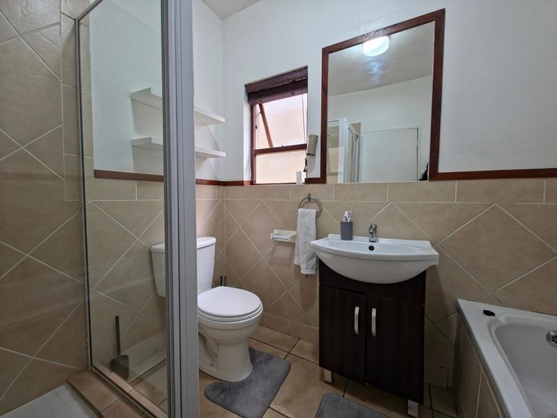 A functional bathroom featuring a shower enclosure, bathtub, vanity cabinet with basin, and tiled finishes, offering a practical layout for daily use.