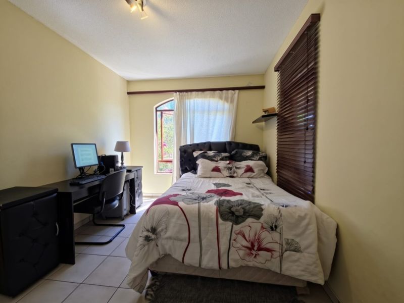 A functional bedroom featuring tiled flooring, an arched window with wooden blinds, and neutral wall finishes.
