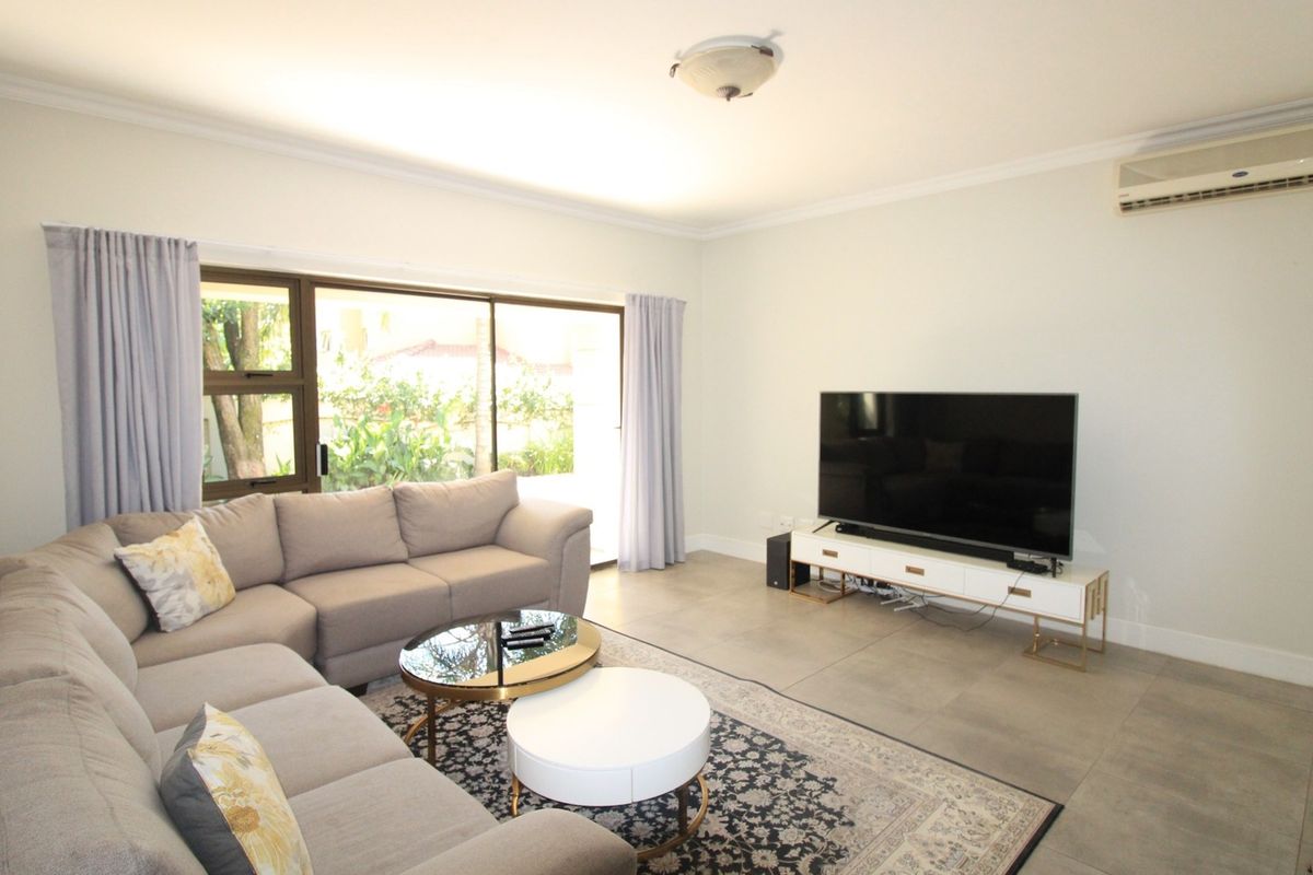 A bright and spacious living room featuring large sliding glass doors, tiled flooring, and a wall-mounted air conditioning unit.