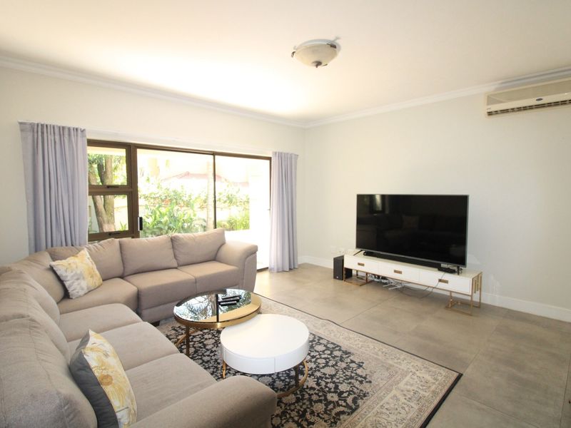 A bright and spacious living room featuring large sliding glass doors, tiled flooring, and a wall-mounted air conditioning unit.