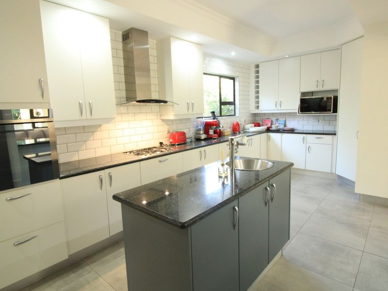 Modern kitchen featuring a central island, granite countertops, subway tile backsplash, built-in appliances, and ample cabinetry storage.