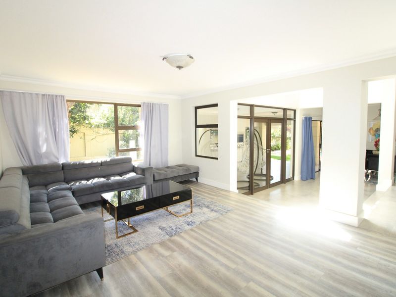 Spacious living room featuring modern laminate flooring, large aluminium windows, and sliding doors providing access to the outdoor area.