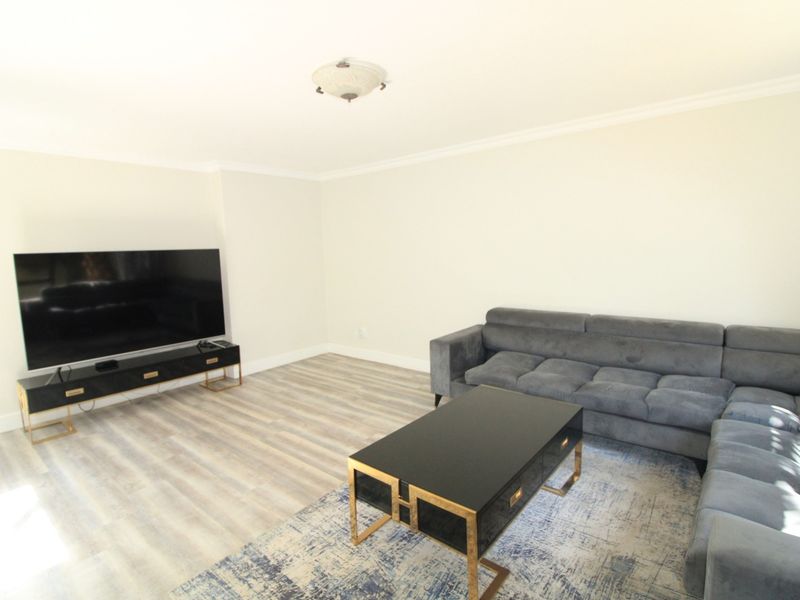 A bright living room featuring modern laminate flooring and clean white walls, providing a neutral and versatile space for relaxation.