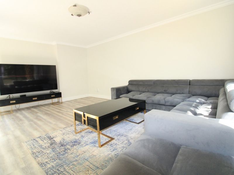 A bright and spacious living room featuring modern laminate flooring and clean, neutral wall finishes.