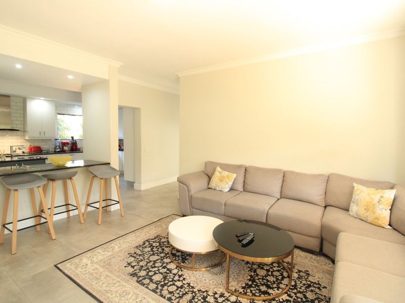 An open-plan living area featuring a modern kitchen with a breakfast bar, granite countertops, and neutral tiled flooring throughout.