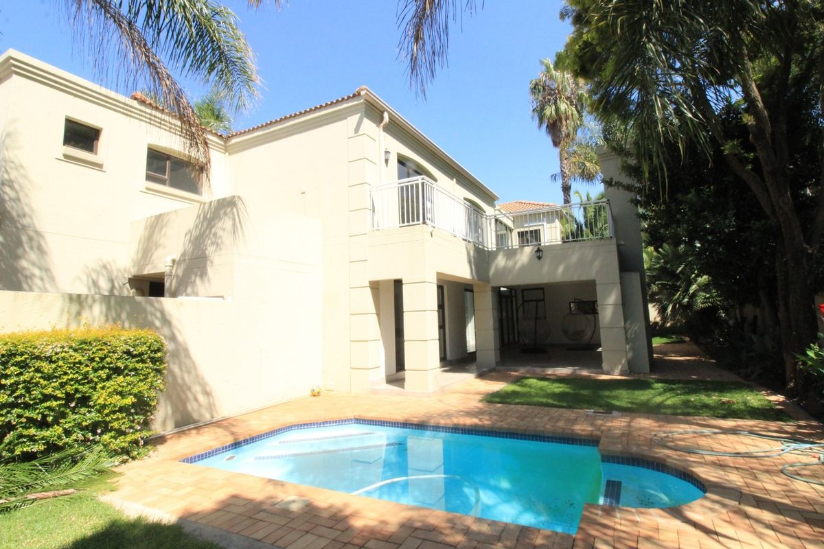 Rear view of the house featuring a swimming pool, brick-paved patio area, and an upper-level balcony with metal railings.