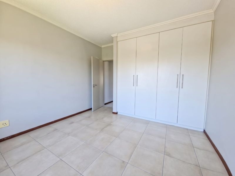 A bright, empty bedroom featuring neutral tiled flooring, coved ceilings, and ample built-in cupboard storage space.