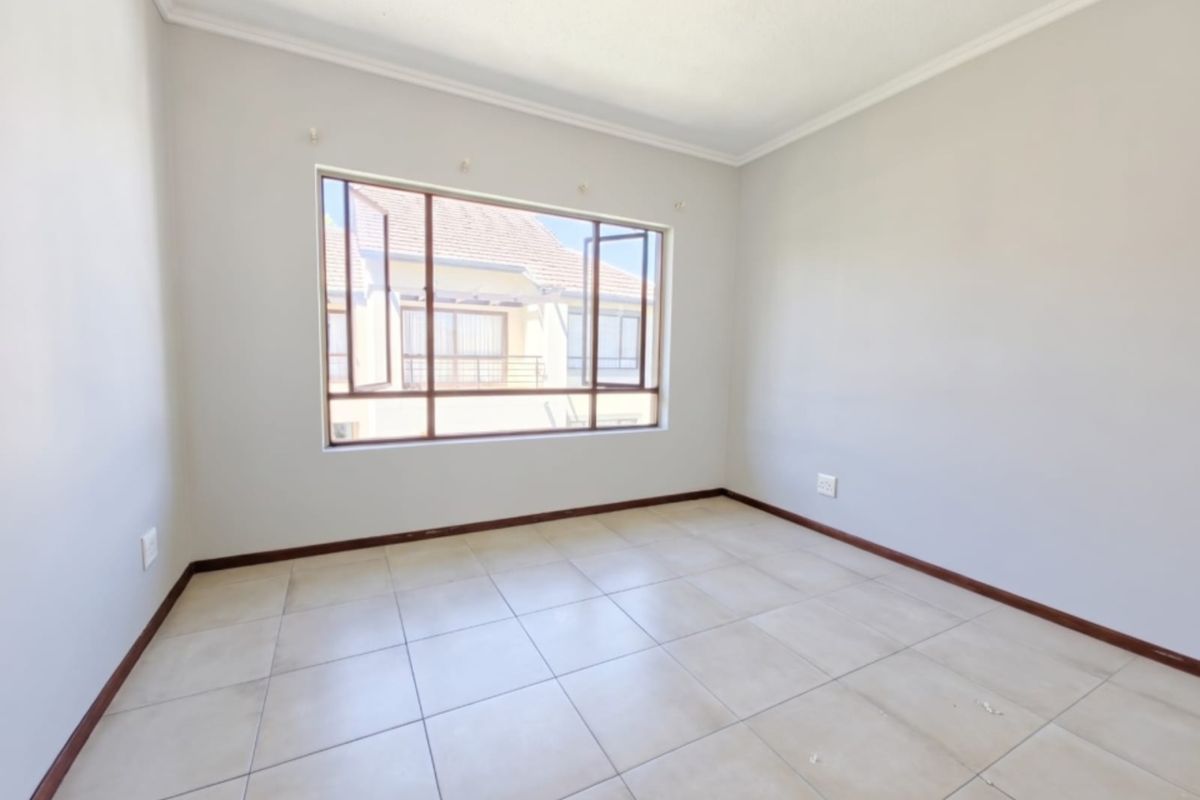 A bright, empty bedroom featuring neutral tiled flooring, clean walls, and a large window providing natural light.