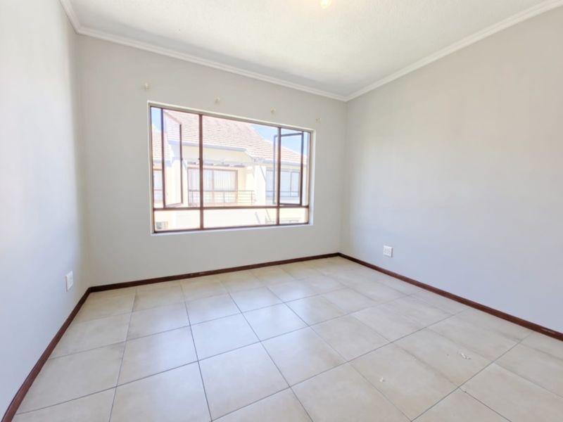 A bright, empty bedroom featuring neutral tiled flooring, clean walls, and a large window providing natural light.