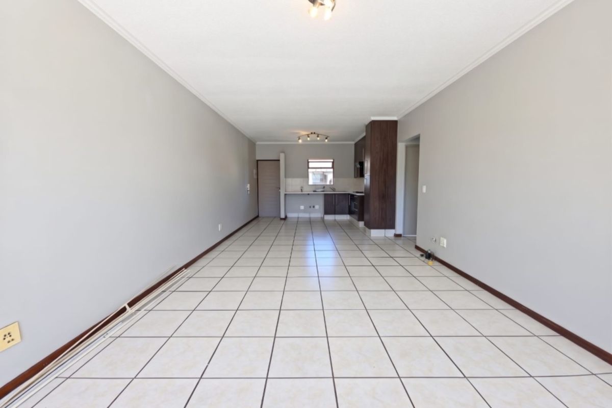 Spacious open-plan living and kitchen area featuring neutral wall tones, tiled flooring, and functional kitchen cabinetry in a well-maintained apartment setting.