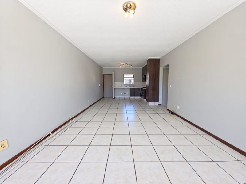 Spacious open-plan living and kitchen area featuring neutral wall tones, tiled flooring, and functional kitchen cabinetry in a well-maintained apartment setting.