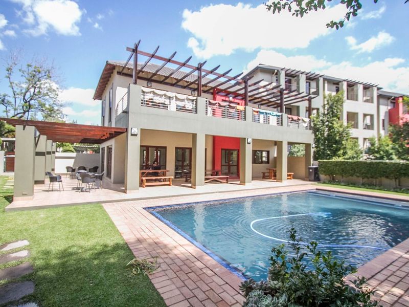 A well-maintained communal pool area featuring a covered patio, timber pergola, and landscaped garden space within an apartment complex.