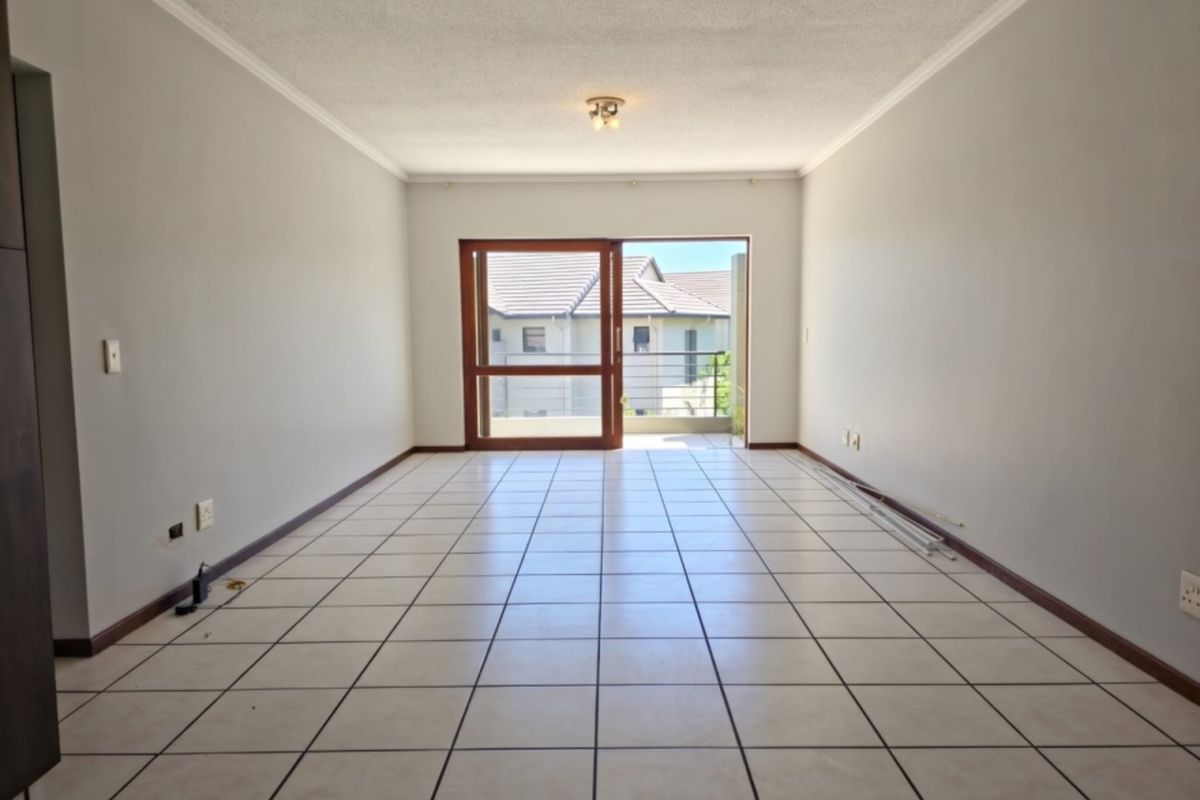 A spacious, empty living area featuring neutral tiled flooring and a large sliding glass door providing access to an outdoor balcony.