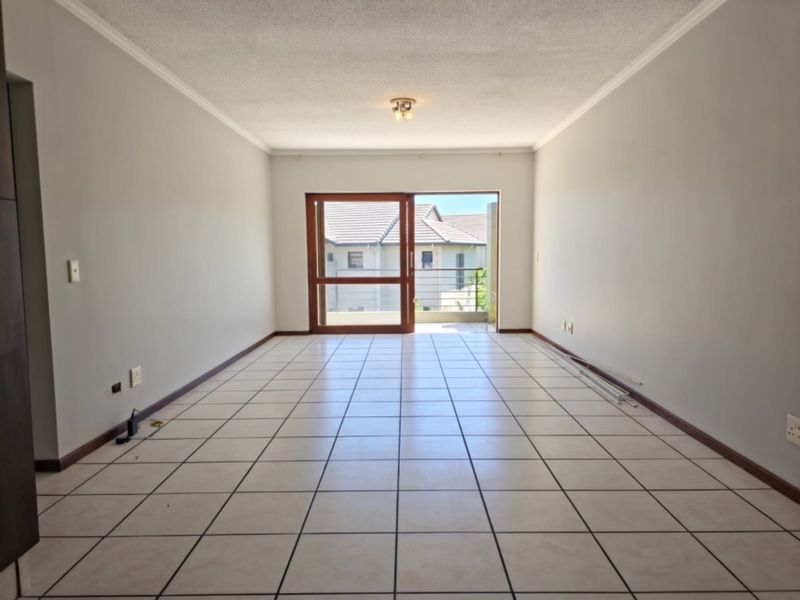 A spacious, empty living area featuring neutral tiled flooring and a large sliding glass door providing access to an outdoor balcony.