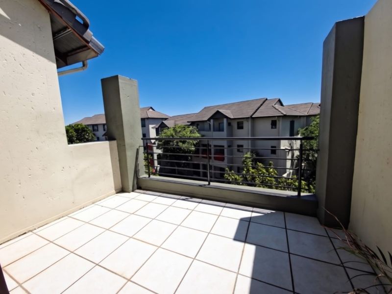 A spacious open-air balcony featuring tiled flooring and a secure metal balustrade, offering a clear view of the surrounding apartment complex.