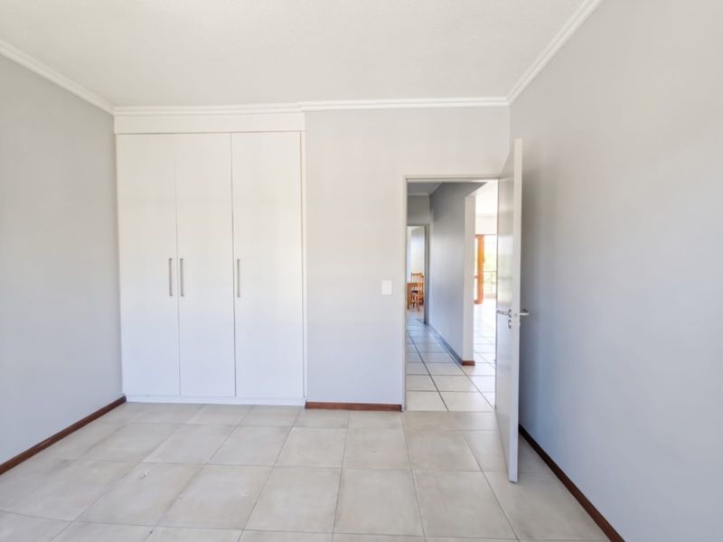 A bright, empty bedroom featuring neutral tiled flooring, built-in white cupboards, and clean wall finishes, offering a versatile space ready for personalization.