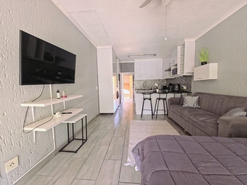 Open-plan living area featuring a compact kitchen with white cabinetry, tiled flooring, and a breakfast counter, creating a functional and connected living space.