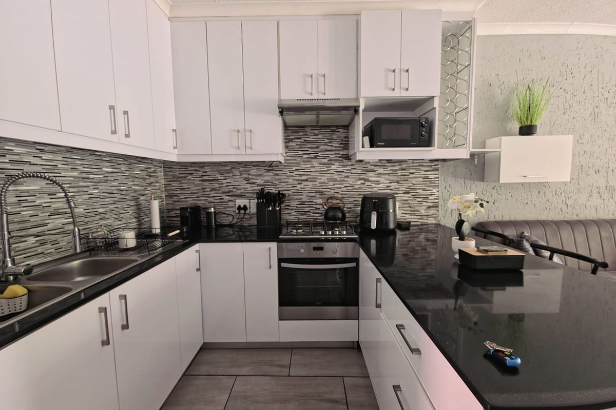 Modern kitchen featuring white cabinetry, black granite countertops, mosaic tile backsplash, and integrated stainless steel appliances including a gas hob and oven.