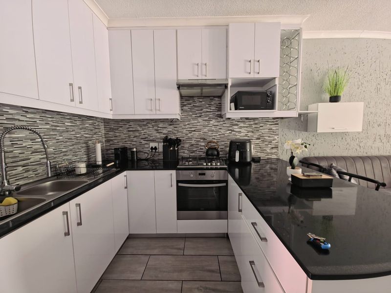 Modern kitchen featuring white cabinetry, black granite countertops, mosaic tile backsplash, and integrated stainless steel appliances including a gas hob and oven.