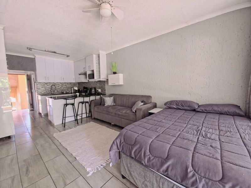 Open-plan studio apartment featuring a compact kitchen with built-in cabinetry, a breakfast bar, and tiled flooring throughout the living and sleeping area.