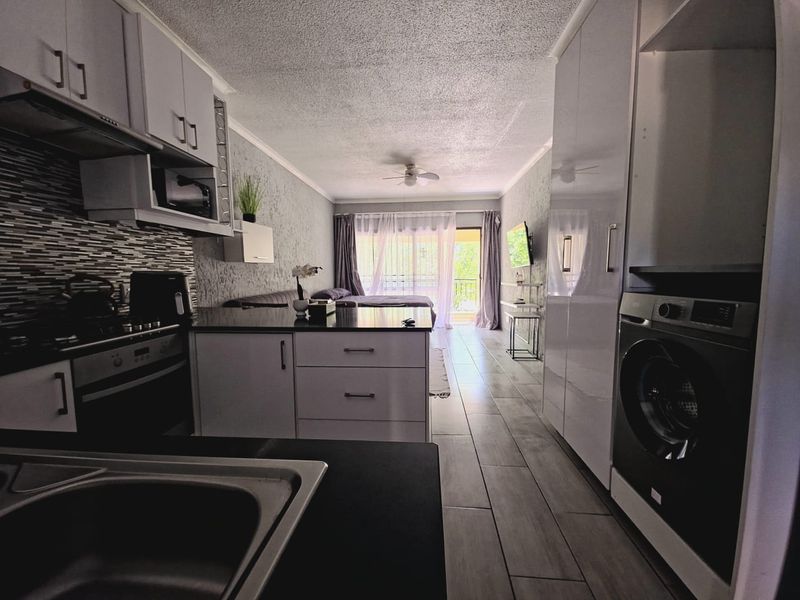 Modern open-plan apartment featuring a sleek kitchen with integrated appliances, stone countertops, and tiled flooring, flowing into a bright living area with balcony access.