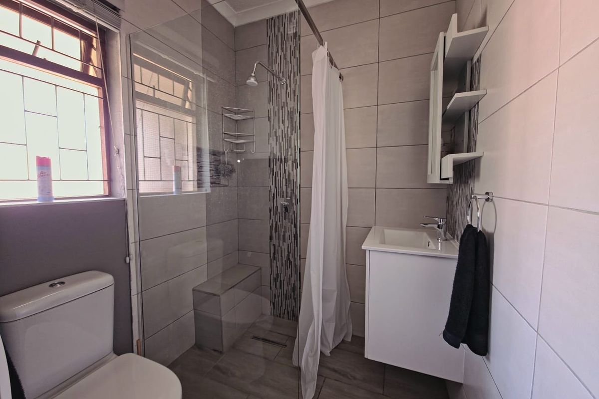 A modern bathroom featuring a walk-in shower with glass screen, vanity basin, and toilet, finished with neutral wall and floor tiling.