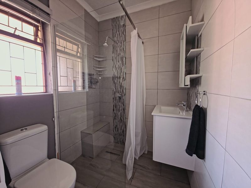 A modern bathroom featuring a walk-in shower with glass screen, vanity basin, and toilet, finished with neutral wall and floor tiling.