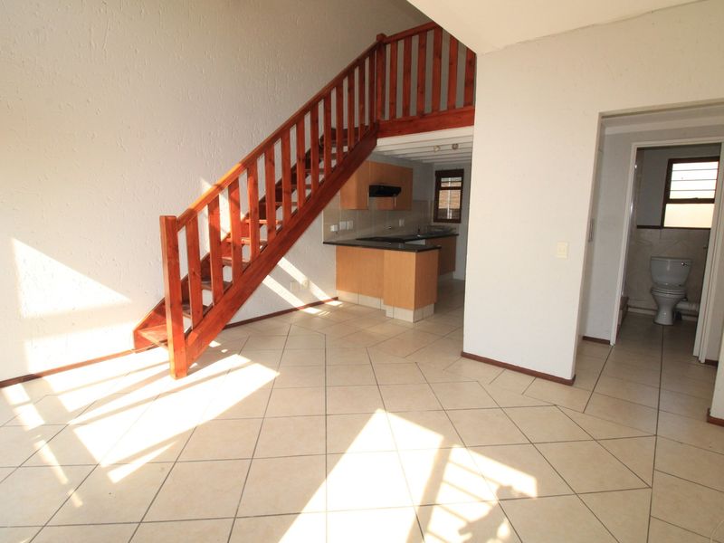 Open-plan living area featuring a wooden staircase, tiled flooring, and an integrated kitchen, with an adjacent bathroom visible.