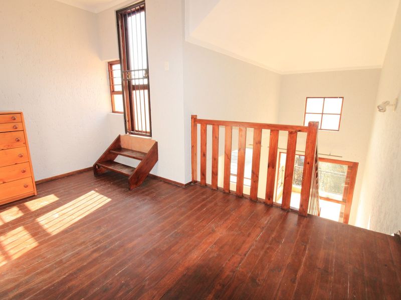 An open-plan mezzanine area featuring polished wooden flooring, a wooden staircase railing, and natural light through casement windows.