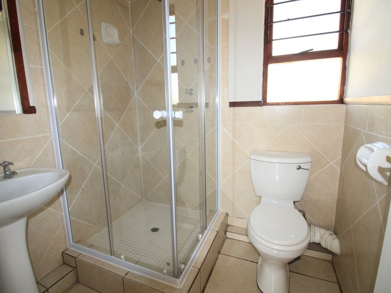 A functional bathroom featuring a shower enclosure, pedestal basin, and toilet with tiled finishes and a louvre window for ventilation.