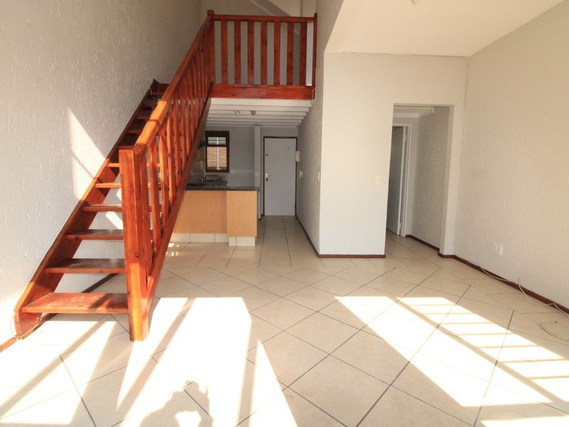 Open plan living area featuring tiled flooring and a wooden staircase leading to an upper level, with an integrated kitchen space.