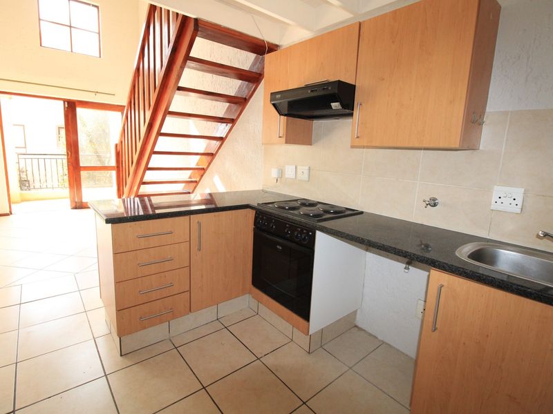 Open plan kitchen featuring wooden cabinetry, granite countertops, and integrated appliances, adjacent to a staircase leading to the upper level.