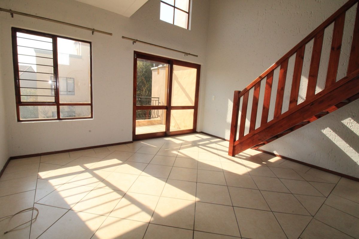 Spacious, light-filled living area featuring tiled floors, a double-volume ceiling, and a wooden staircase leading to the upper level.