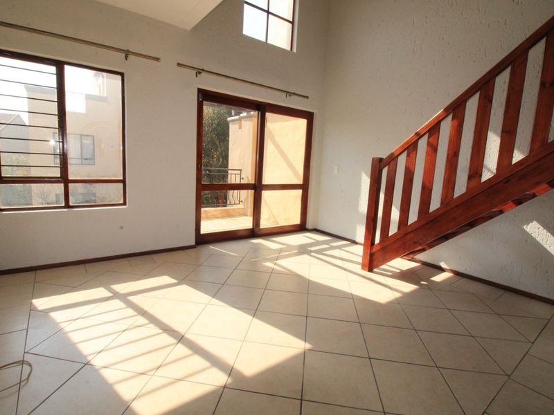 Spacious, light-filled living area featuring tiled floors, a double-volume ceiling, and a wooden staircase leading to the upper level.