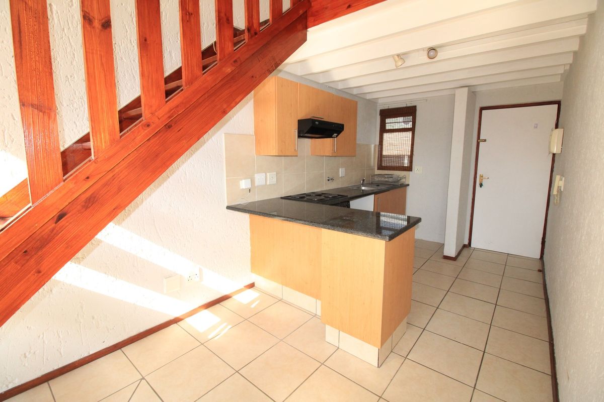 Compact kitchen featuring light wood cabinetry, granite countertops, electric hob, and tiled flooring, situated beneath an exposed timber staircase.