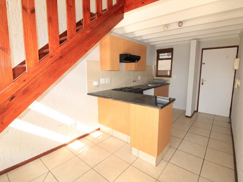 Compact kitchen featuring light wood cabinetry, granite countertops, electric hob, and tiled flooring, situated beneath an exposed timber staircase.
