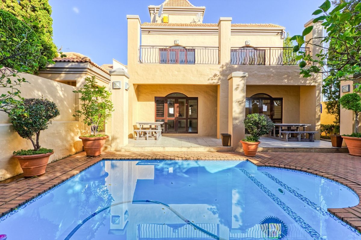 Rear view of the property featuring a swimming pool, paved patio area, and an upper-level balcony with wrought iron railings.
