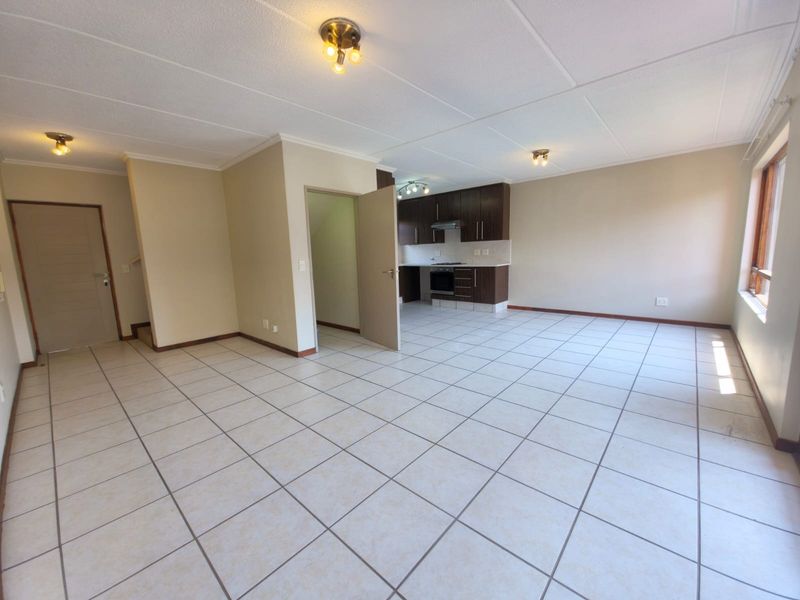 Spacious open-plan living area featuring tiled flooring and a functional kitchen with built-in cabinetry, oven, and hob, offering a clean, blank canvas.