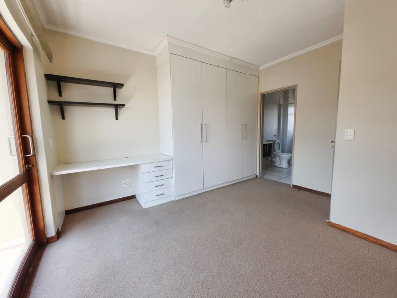 A spacious bedroom featuring built-in cupboards, a fitted desk with shelving, and direct access to an en-suite bathroom.